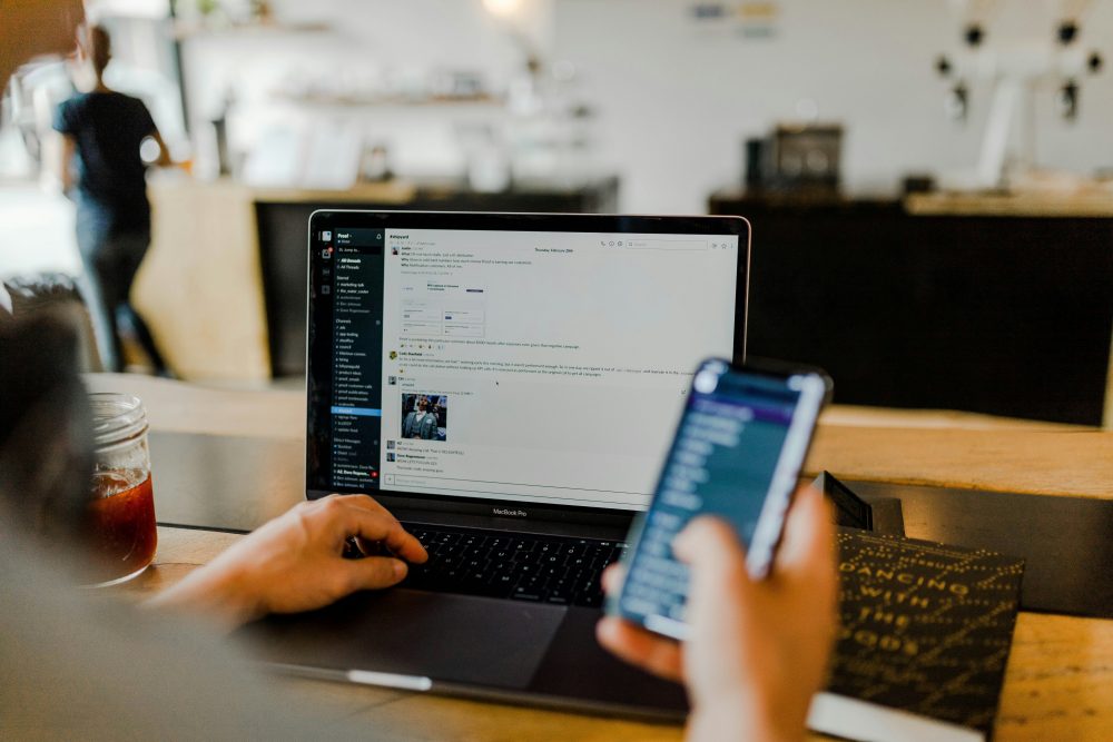 Mann vor dem Laptop hält Smartphone