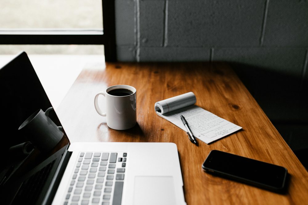 Schreibtisch mit Laptop, Kaffe, Smartphone und Schreibblock